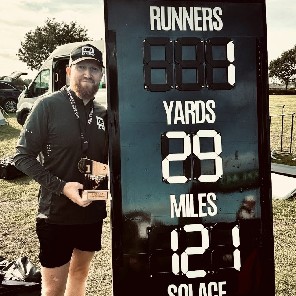 Win at the Solace Backyard Ultra, standing with the finisher board